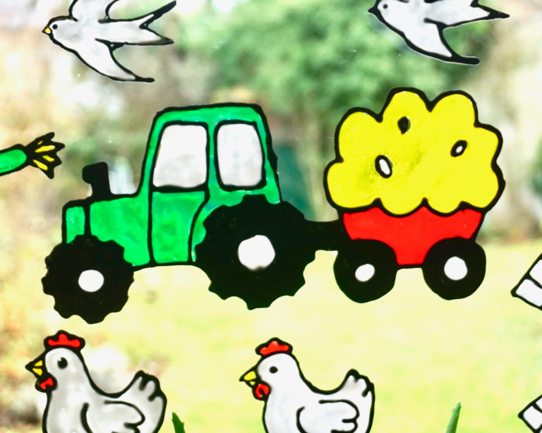 Zöld traktor szénával megrakott piros pótkocsival, közelről